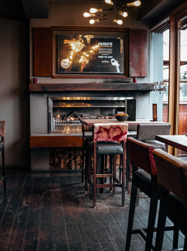 Casa Publica, a South American-inspired bar in Christchurch, features an inviting indoor dining space with a fireplace and bar stools.