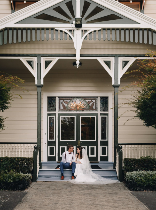 A wedding couple sits on the steps of Caccia Birch House, a beautiful late 19th-century colonial homestead in Manawatū-Whanganui.