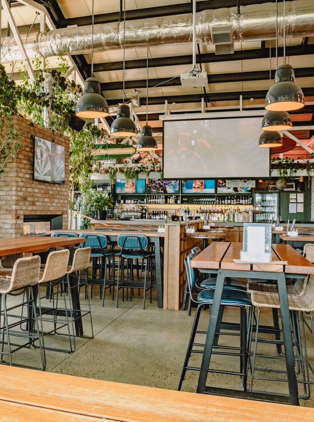 A spacious, contemporary timber and brick gastropub interior with lush greenery at Long Bay Surf Club, Auckland.