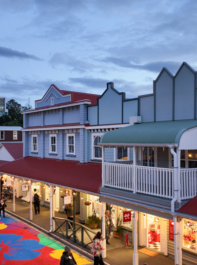 A lively street scene with a colorful painted pathway winds through the quaint, vintage-inspired architecture of The Historic Village, Tauranga.