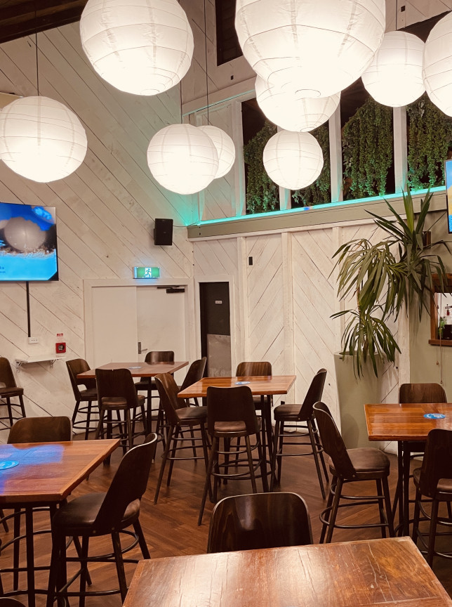 A relaxed, contemporary dining space at The Cambridge Hotel, Wellington, featuring white-washed walls, large lanterns, and wooden tables.