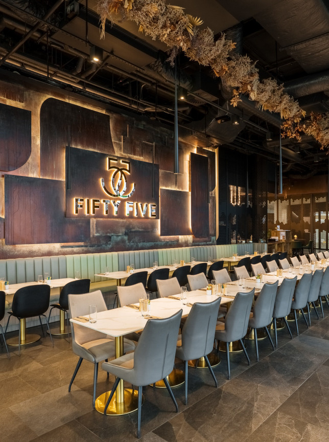 A chic, modern dining area at 55 Cafe in Auckland, featuring long tables, booth seating, and a prominent illuminated 'Fifty Five' sign.