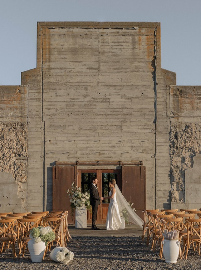 A rustic outdoor wedding ceremony at The Flaxmill, Christchurch, featuring its original industrial concrete walls.