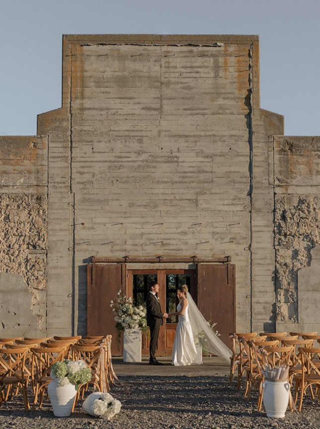 A rustic outdoor wedding ceremony at The Flaxmill, Christchurch, featuring its original industrial concrete walls.
