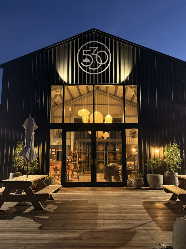 Shed530 Estate, a modern barn-style winery in Hawke's Bay, showing its illuminated interior and outdoor deck at dusk.