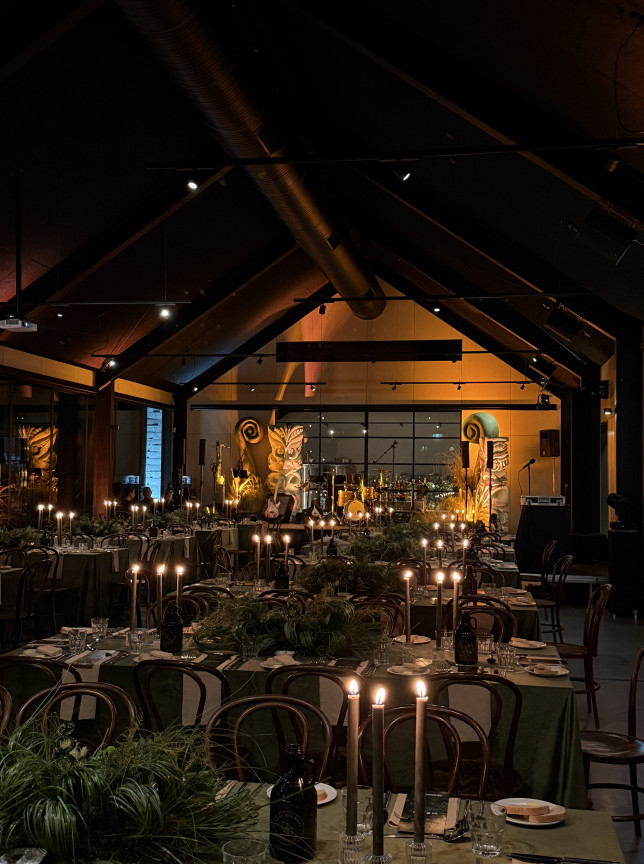 A candlelit private dining room in The Cargo Collective's modern rustic Brew Hall in Queenstown, featuring a stage and brewery backdrop.