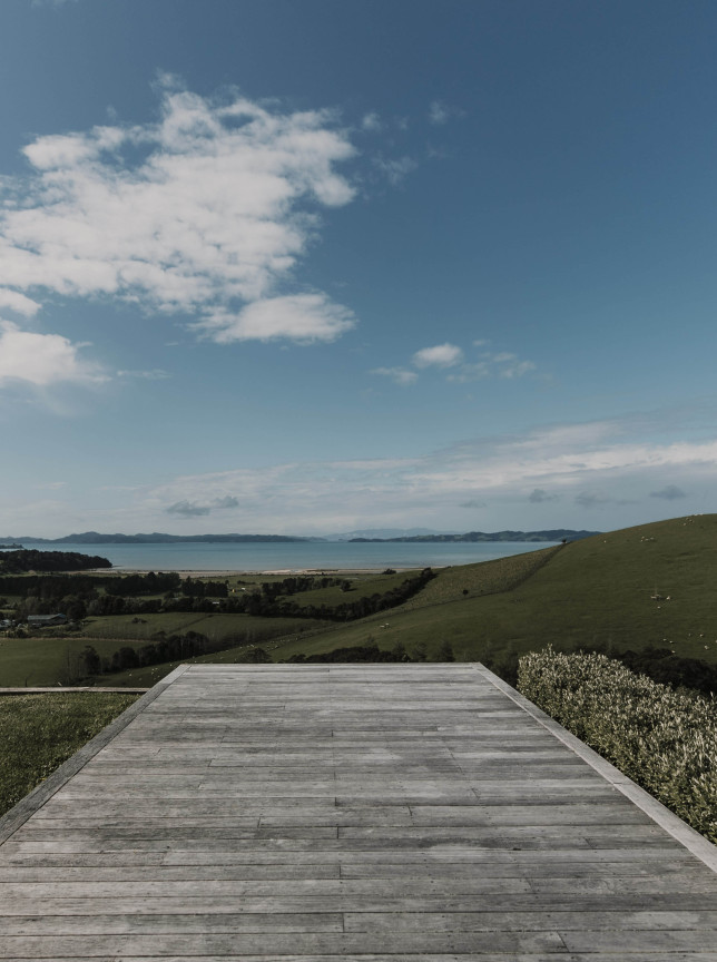 Kauri Bay, Auckland's modern-rustic wooden deck overlooks the scenic Hauraki Gulf and rolling hills.