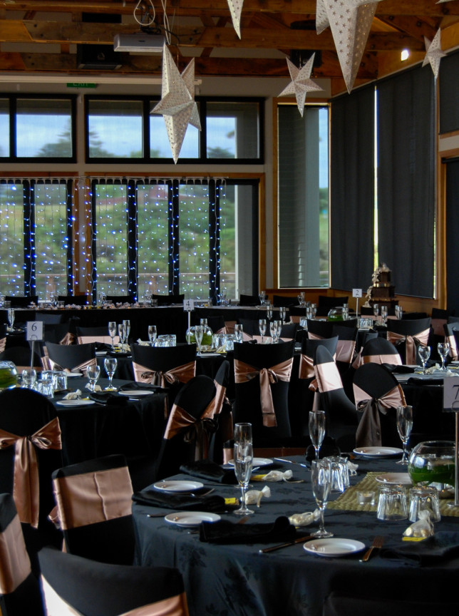 An elegant banquet setup in Butterfly Creek's spacious function room in Auckland, featuring exposed beams and sparkling lights.