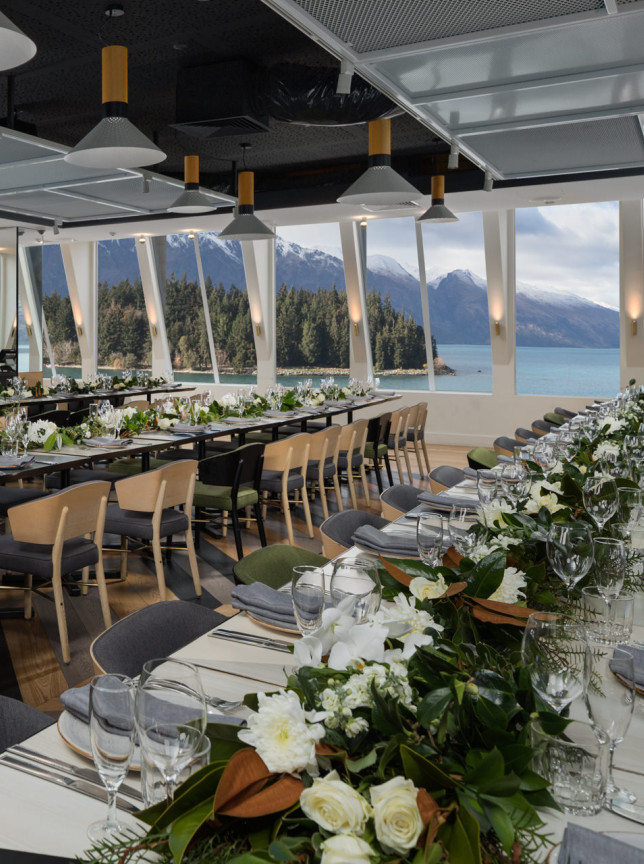 QT Queenstown's alpine-chic dining room features stunning lake and mountain views through floor-to-ceiling windows, set for an elegant event.