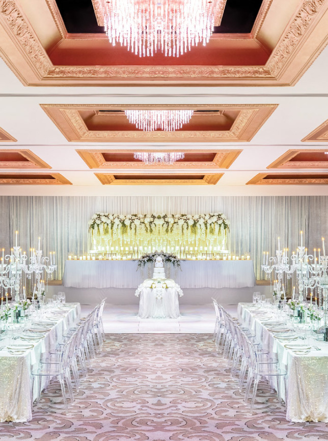 A lavish wedding reception in Cordis, Auckland's classic ballroom, with sparkling chandeliers and white floral decor.