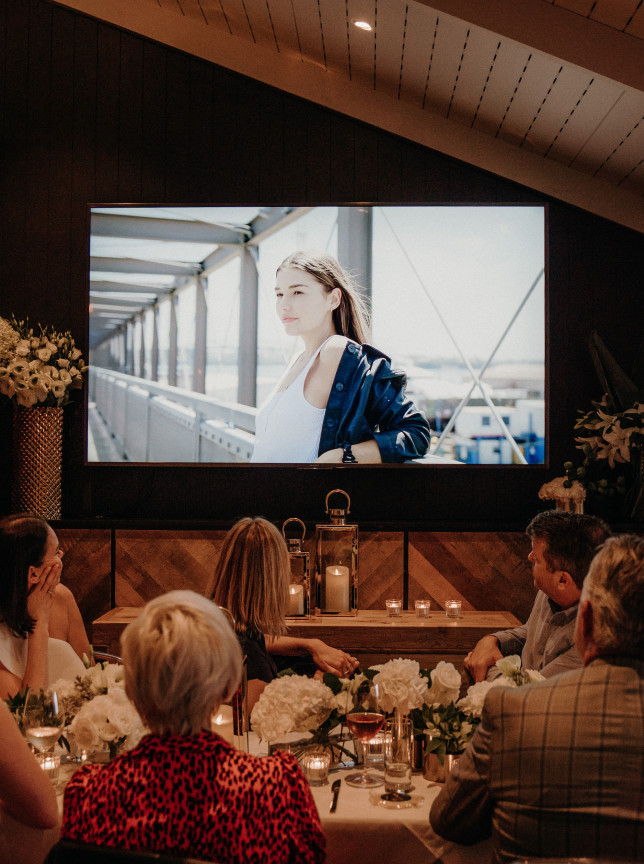 A private dining room at VYC Auckland, showcasing a modern, elegant design with wooden accents and a large screen for presentations.