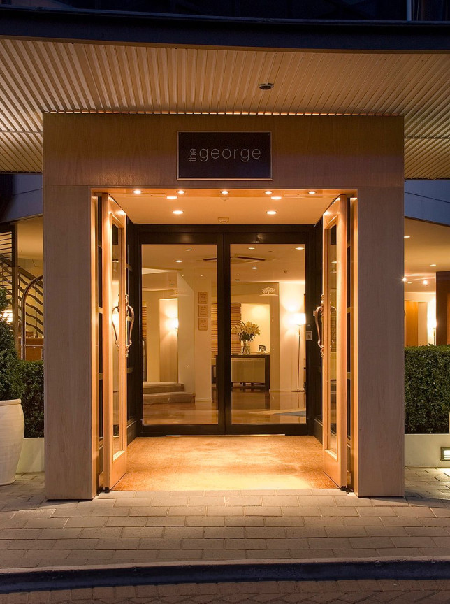 Illuminated entrance of The George, a contemporary luxury boutique hotel in Christchurch, featuring stone pillars and glass doors.