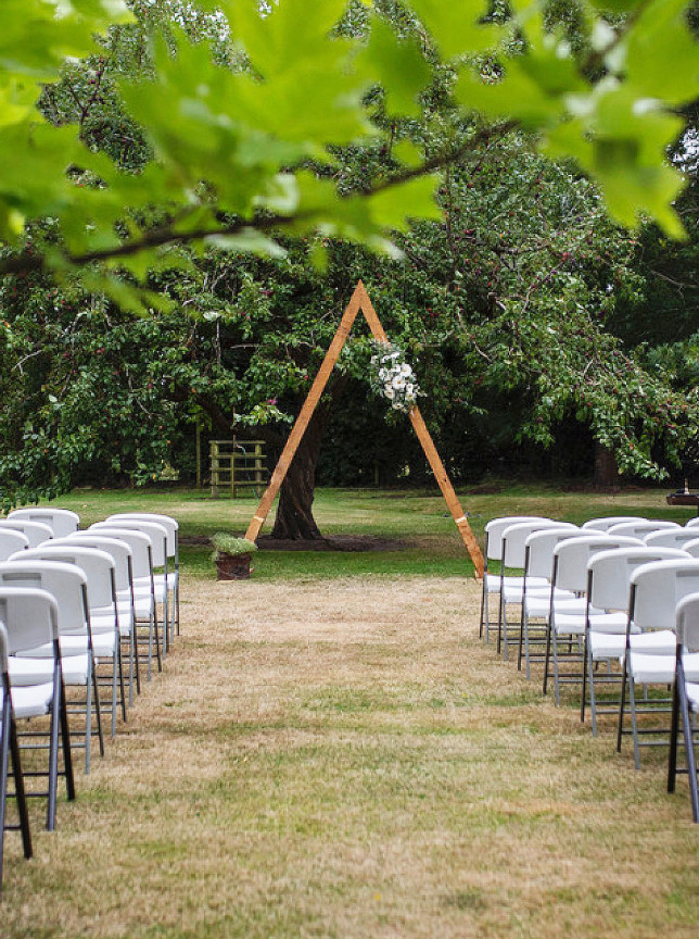 An outdoor ceremony setup featuring a rustic arch and white chairs in the country gardens of Omarino Estate, Christchurch.