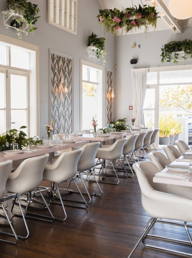 Moxie, a modern eatery set in a charming Auckland villa, features a vibrant dining room with pastel tables and lush floral accents.