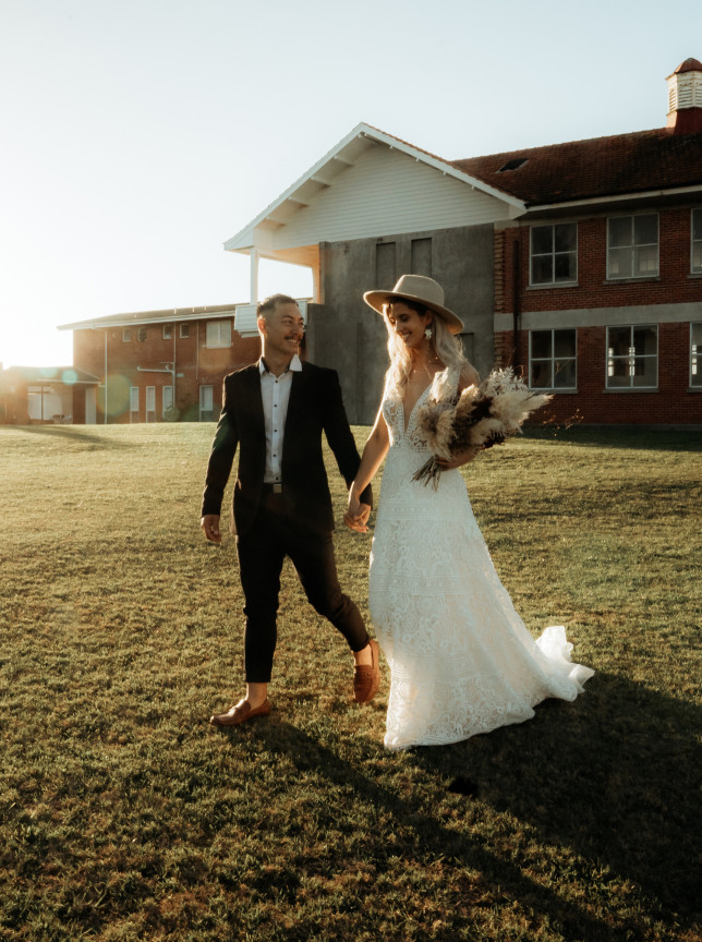 A wedding couple walks hand-in-hand across the sprawling lawn of LaValla Estate, a historic schoolhouse venue near Auckland.