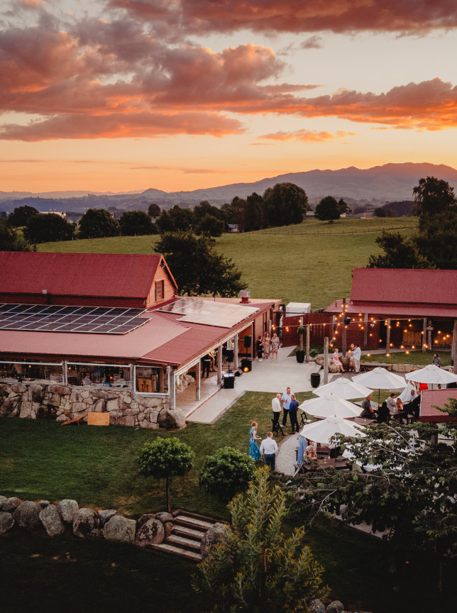 An outdoor gathering at The Red Barn, Hamilton's rustic barn-style heritage venue, illuminated by a vibrant sunset.