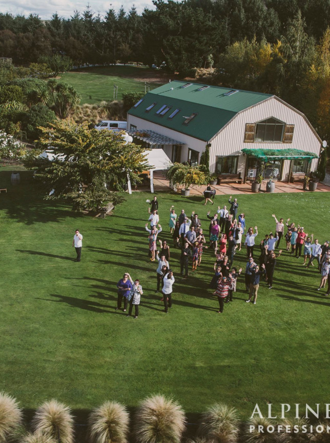 A vibrant outdoor gathering takes place on the sweeping lawn of The Lookout Lodge, a modern barn-style venue in Wanaka.