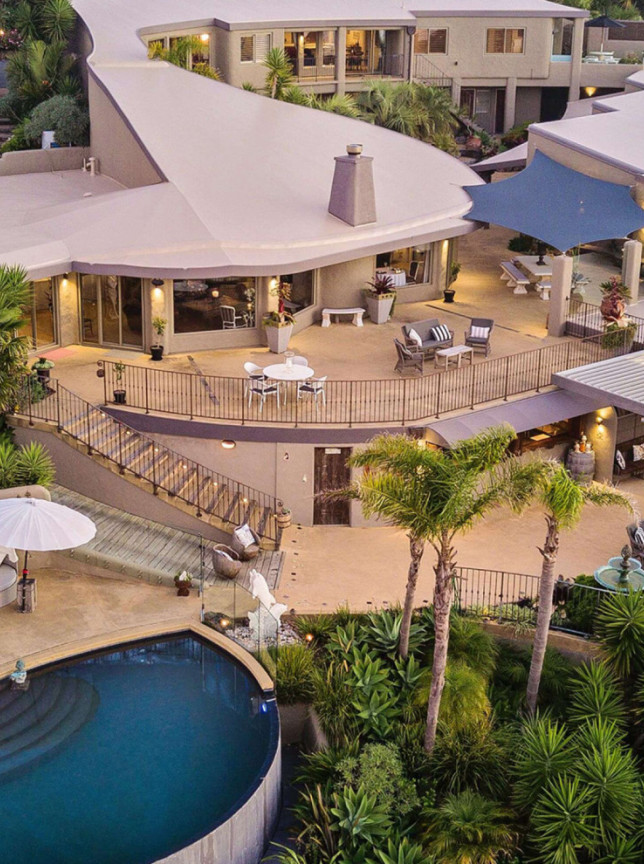 Delamore Lodge on Waiheke Island features multi-level outdoor decks and an infinity pool, with architecture resembling a Maori fish hook.