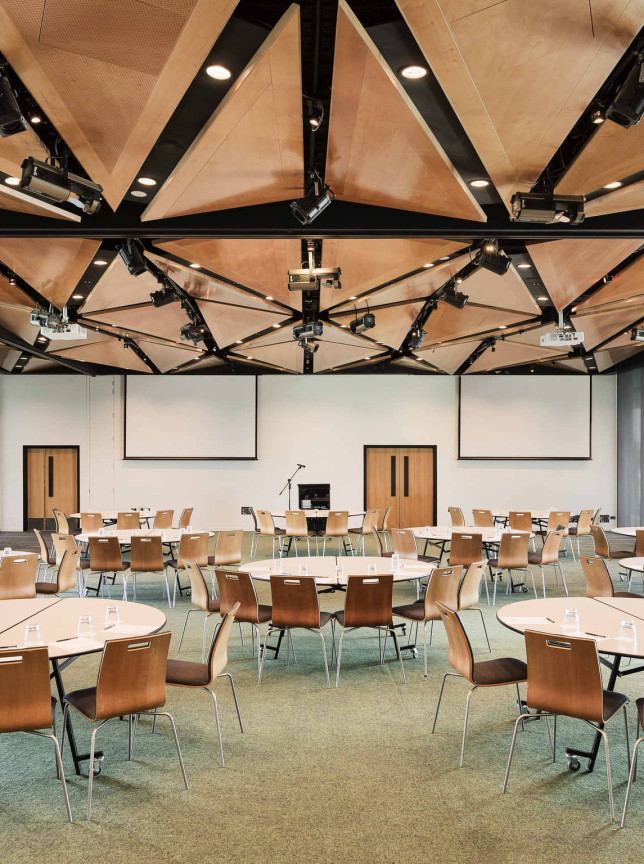 A contemporary conference room at Novotel Auckland Airport, featuring a dramatic New Zealand-inspired geometric timber ceiling and tables set for a meeting.