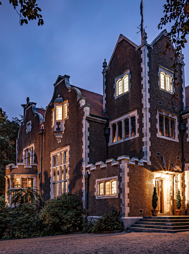 The illuminated Jacobean-style exterior of Olveston Historic Home in Dunedin glows at twilight.