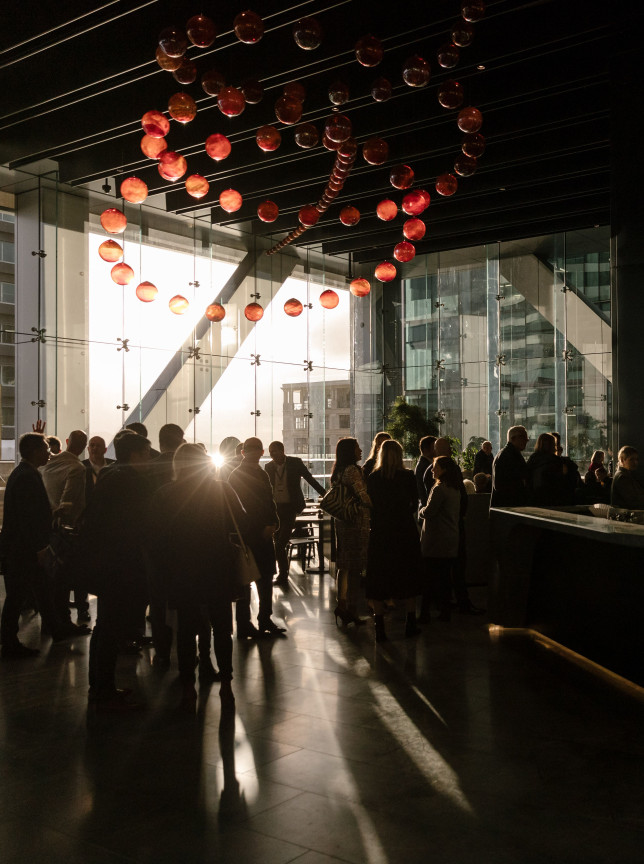 Guests gather at SPECTRA, a modern, glass-enclosed bar and event space in Auckland, featuring city views and unique lighting.