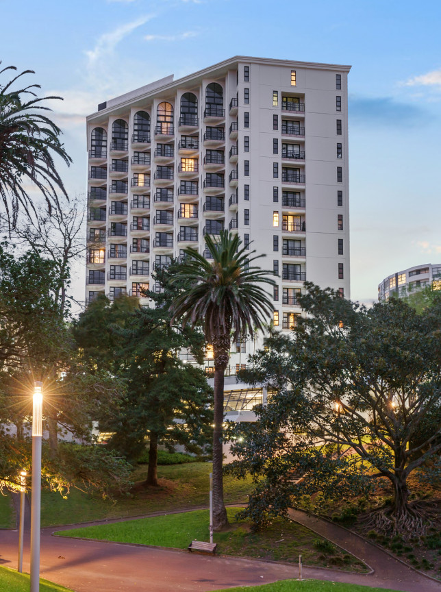 A modern, apartment-style building, the Parkside Hotel and Apartments in Auckland overlooks a green park lit by evening glow.