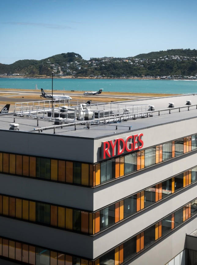 The modern exterior of Rydges Wellington Airport, an integrated airport hotel, overlooks the runway and scenic bay.