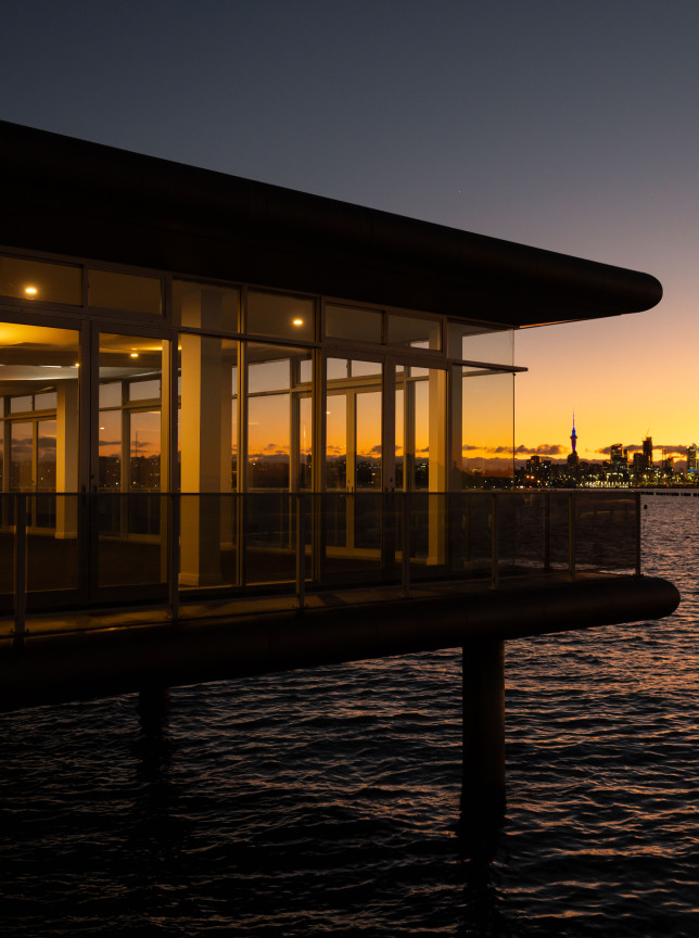 OKAHU in Auckland offers a modern waterfront event space with panoramic glass walls, overlooking the city skyline at sunset.