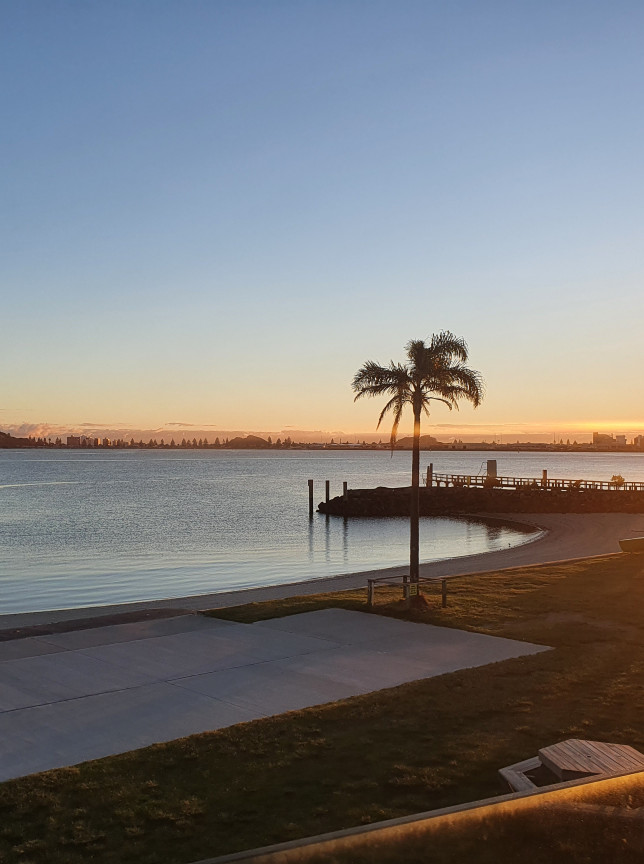 The Yacht Club in Tauranga offers panoramic waterfront views of the harbour and Mount Maunganui from its modern outdoor setting at sunrise.