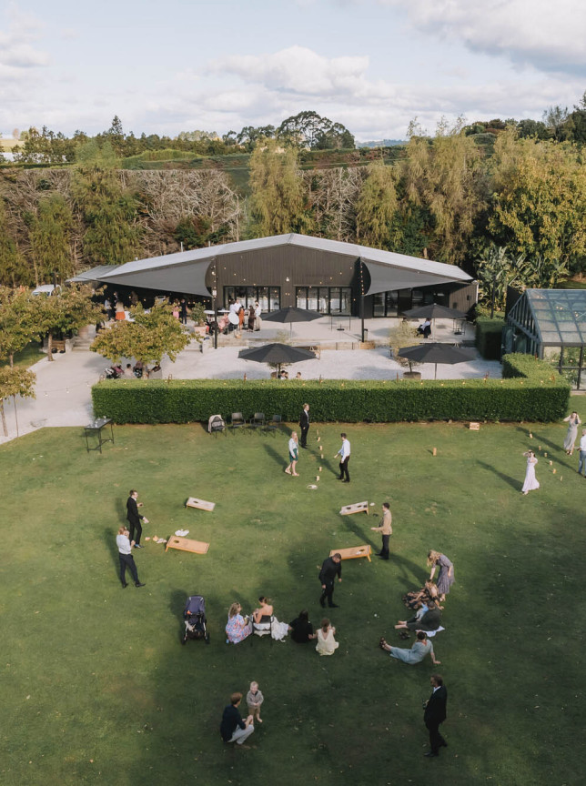 Guests enjoy lawn games on the expansive grounds of Black Walnut, Tauranga, with its modern barn and elegant glasshouse.