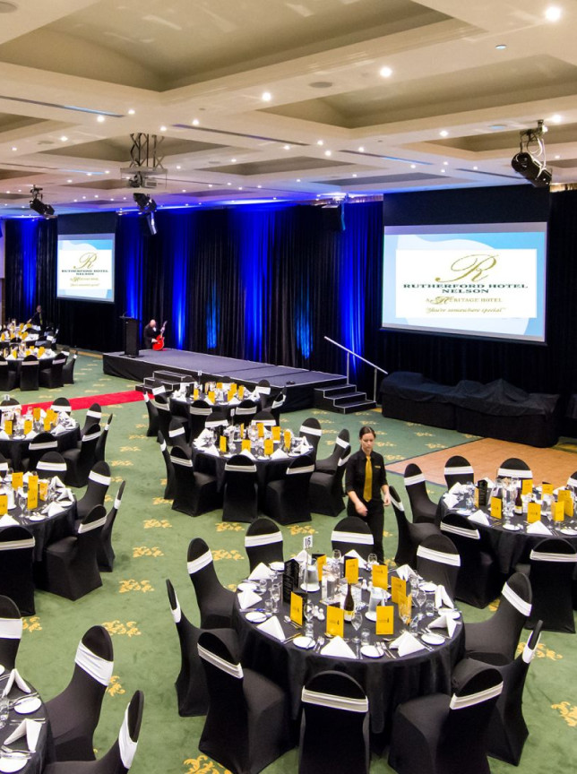 Rutherford Hotel Nelson's modern conference room is set up for a banquet event with numerous round tables and a stage.