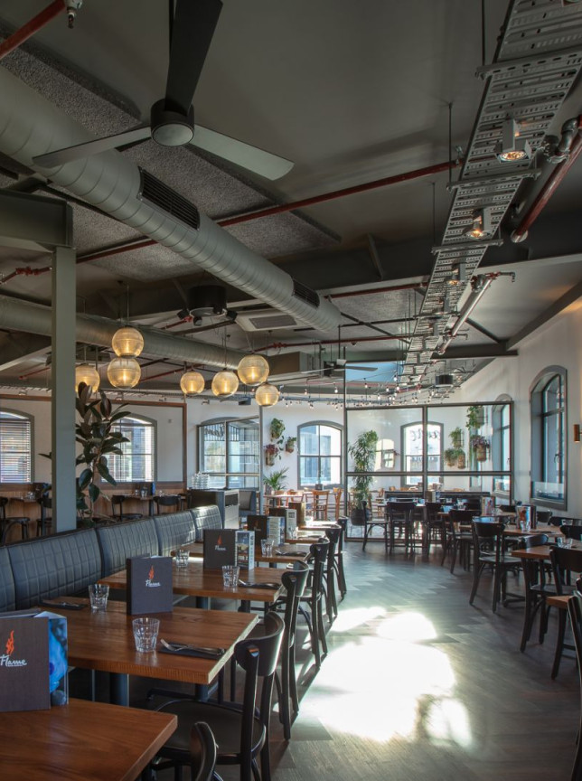 The industrial-chic dining room at Flame Bar & Grill in Queenstown features exposed ductwork, a vibrant bar, and warm lighting.