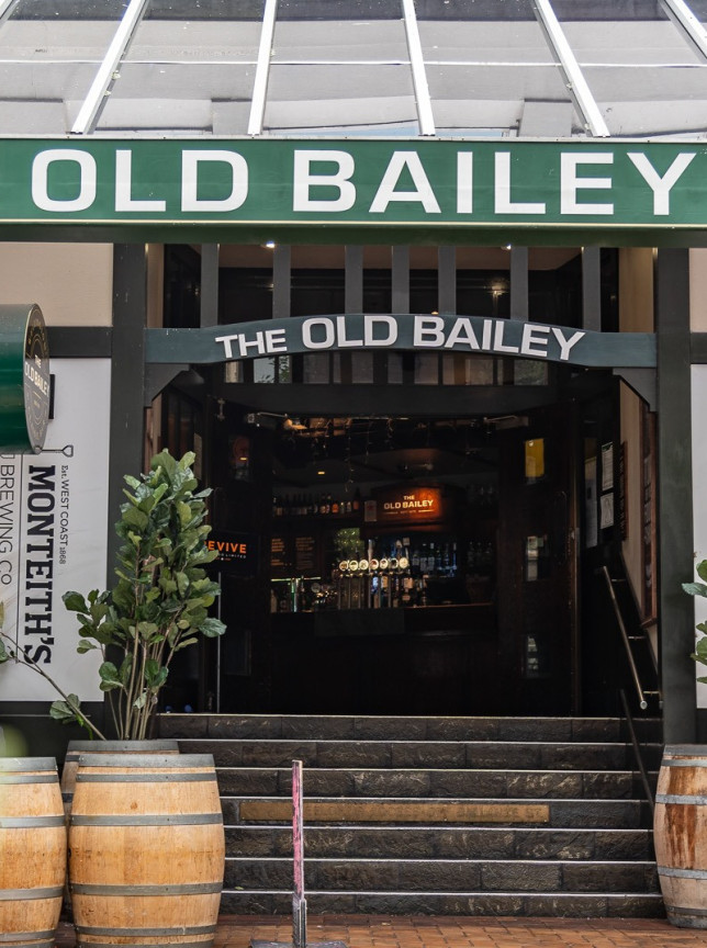 The entrance of The Old Bailey in Wellington, a traditional Kiwi pub, features barrels and steps leading inside.