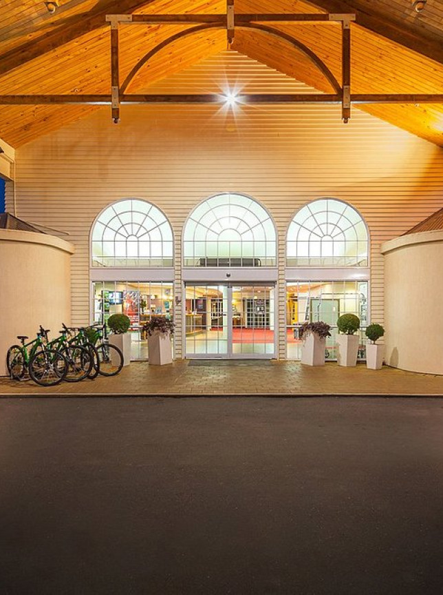 The inviting entrance of Wairakei Resort Taupo at dusk, featuring a grand wooden ceiling and illuminated arched windows.