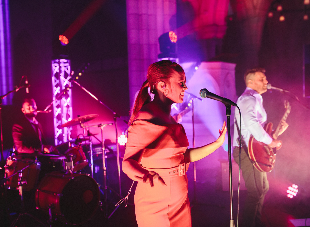 Auckland's Blue Steel band, known for high-energy entertainment, performs with a female vocalist illuminated by vibrant stage lights.