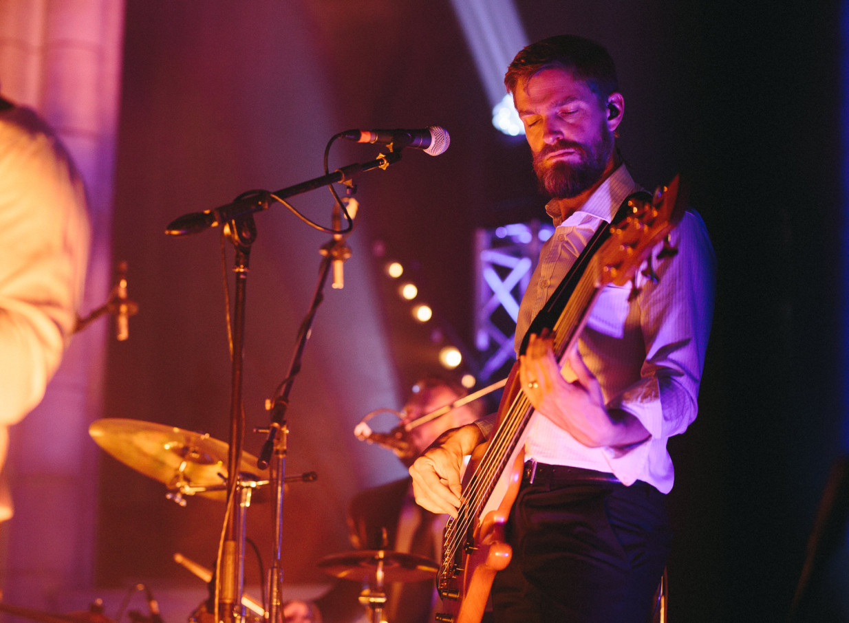 A musician from Auckland's Blue Steel band plays bass guitar with closed eyes during a vibrant live performance.