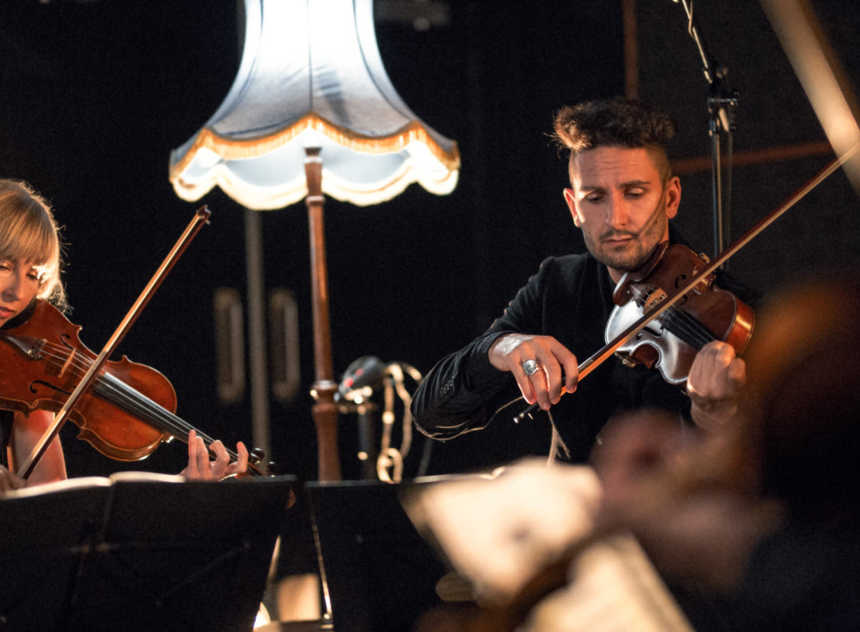The Black Quartet, an Auckland-based contemporary string ensemble, performs with violins under a softly lit, elegant lamp.