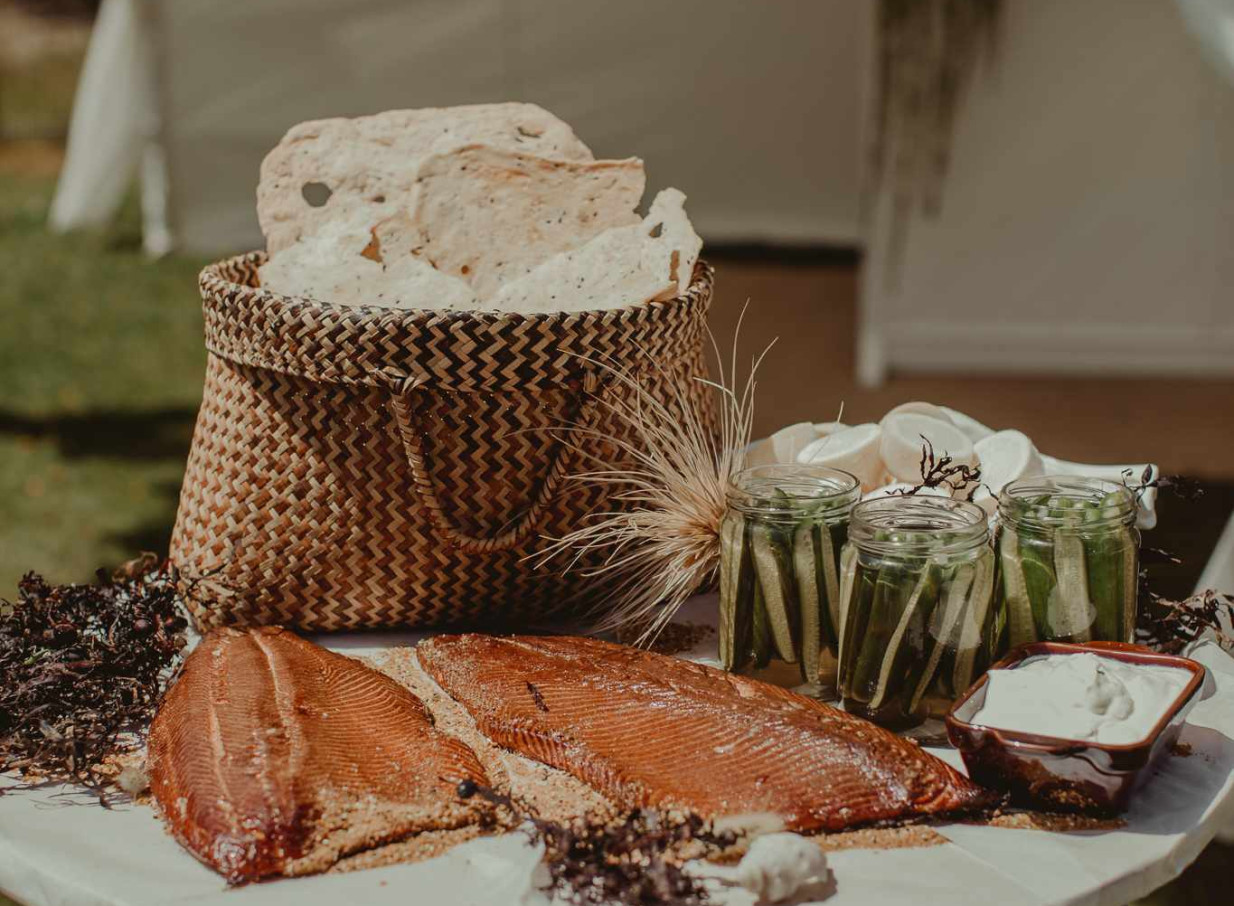 A rustic-chic catering display by Source Kitchen Auckland features cured salmon, crispbreads in a woven basket, and pickled vegetables.