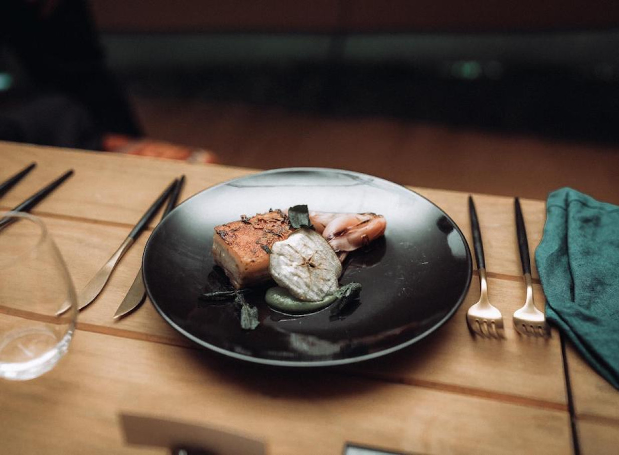 A beautifully plated bespoke meal by Source Kitchen Auckland, featuring roasted meat, vegetables, and sauce on a dark plate.