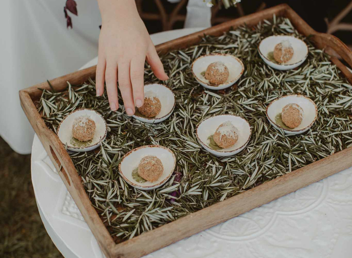 A hand reaches for a gourmet appetizer, elegantly presented with fresh rosemary, from Source Kitchen's bespoke catering in Auckland.