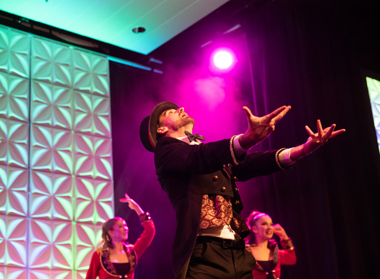 A Finesse Entertainment showman dazzles in a themed performance on a vibrantly lit stage in Auckland.