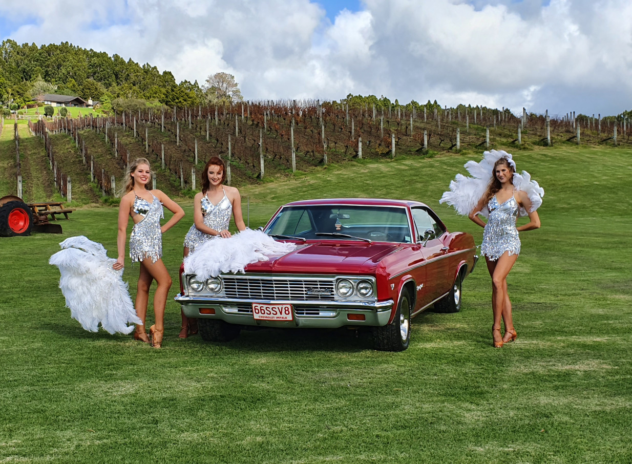 Finesse Entertainment's showgirls pose with a vintage car at a scenic Auckland vineyard.