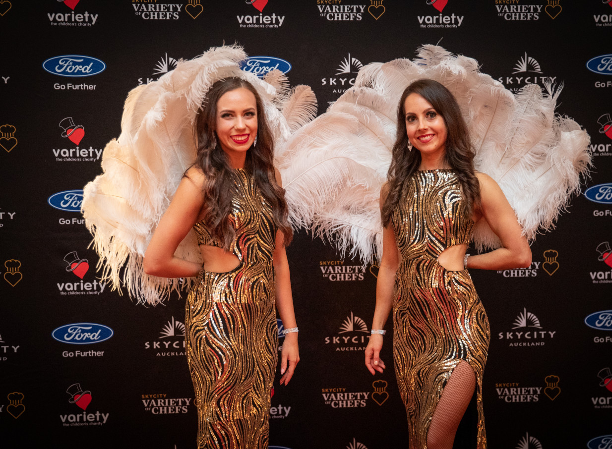 Two glamorous Finesse Entertainment performers from Auckland, in sequined dresses and feather wings, at an event.