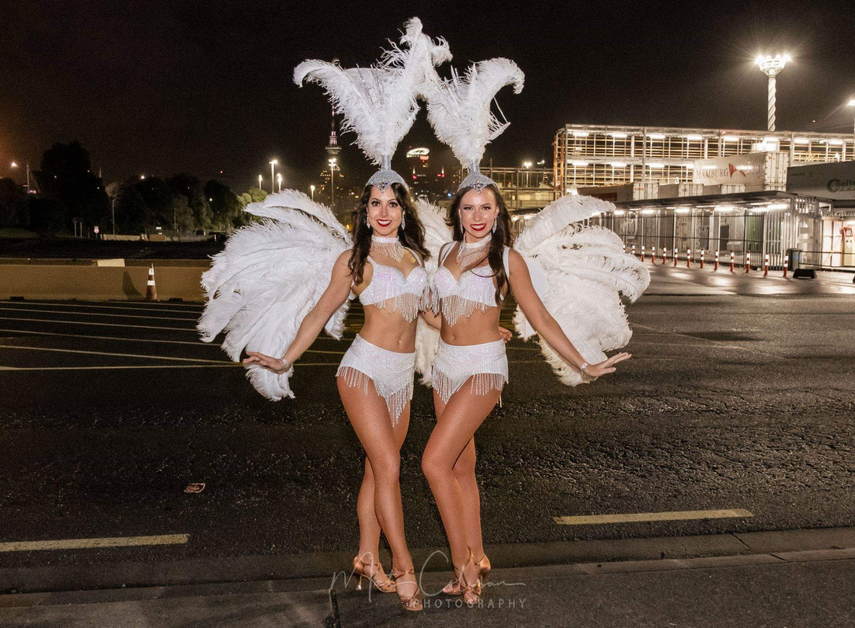 Finesse Entertainment's dazzling showgirls in ornate white costumes perform with Auckland's Sky Tower illuminated in the background.