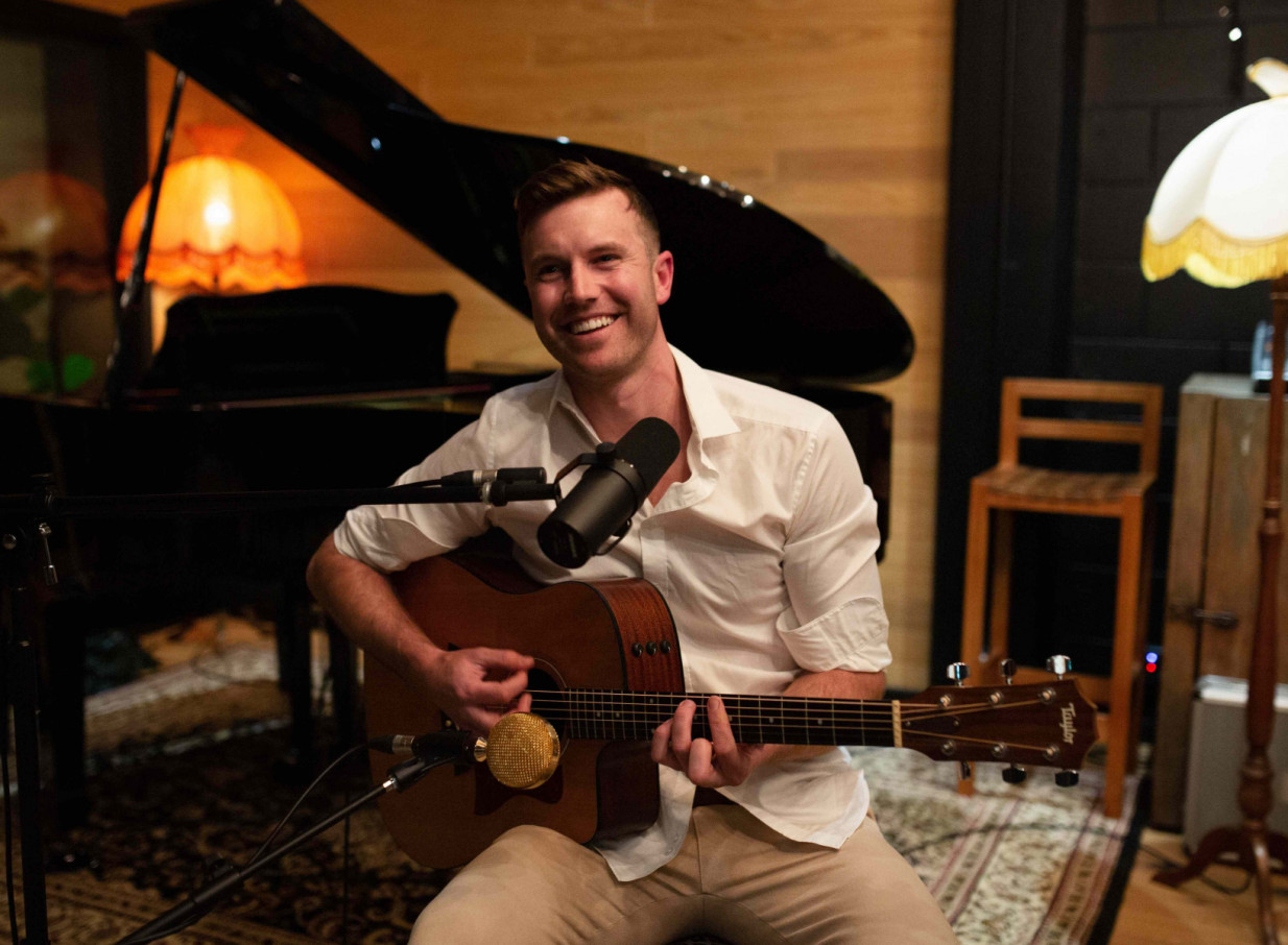 Auckland-based artist Daniel John performs acoustic guitar in a warm studio setting.