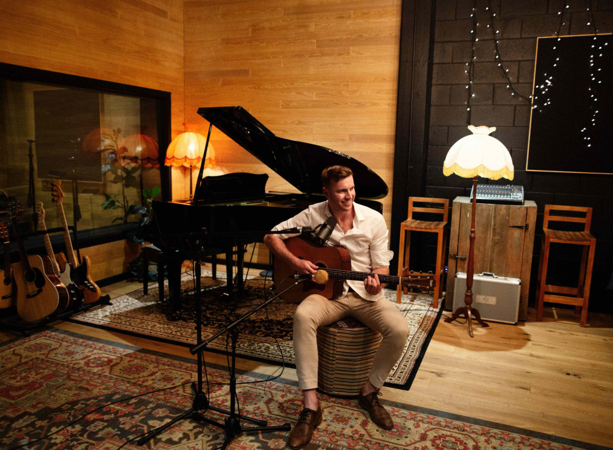 Daniel John performs an acoustic set in a warm, wood-paneled recording studio with industrial accents in Auckland.