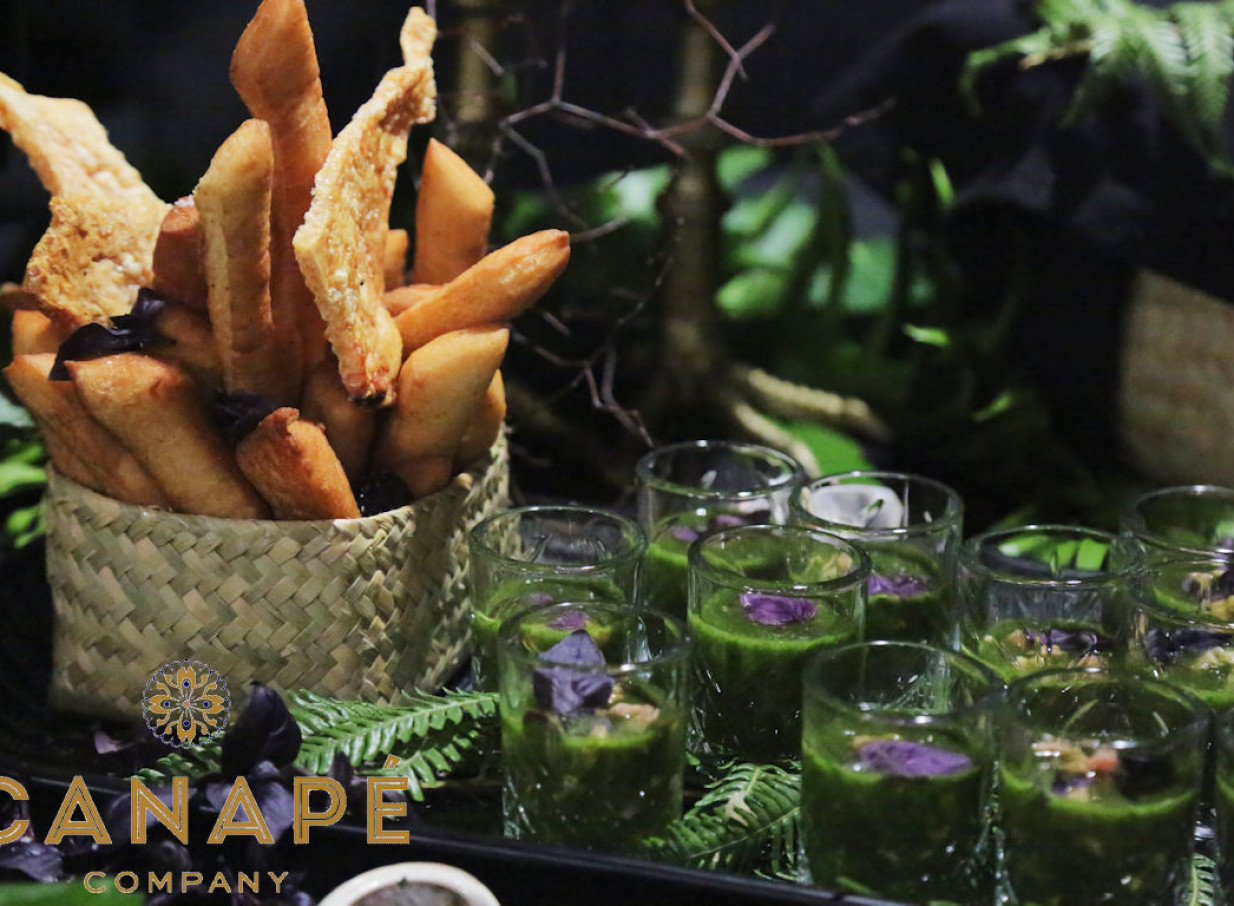 Exquisitely presented fried snacks in a woven basket and vibrant green shooters from Canapé Company, Wellington, showcasing their artful catering.