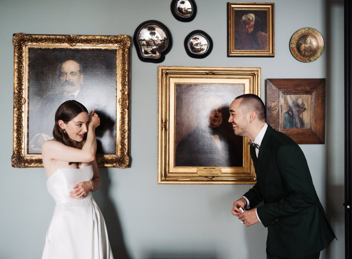 A playful couple shares a moment in a classic art gallery-style room, photographed by Zahn in Auckland.