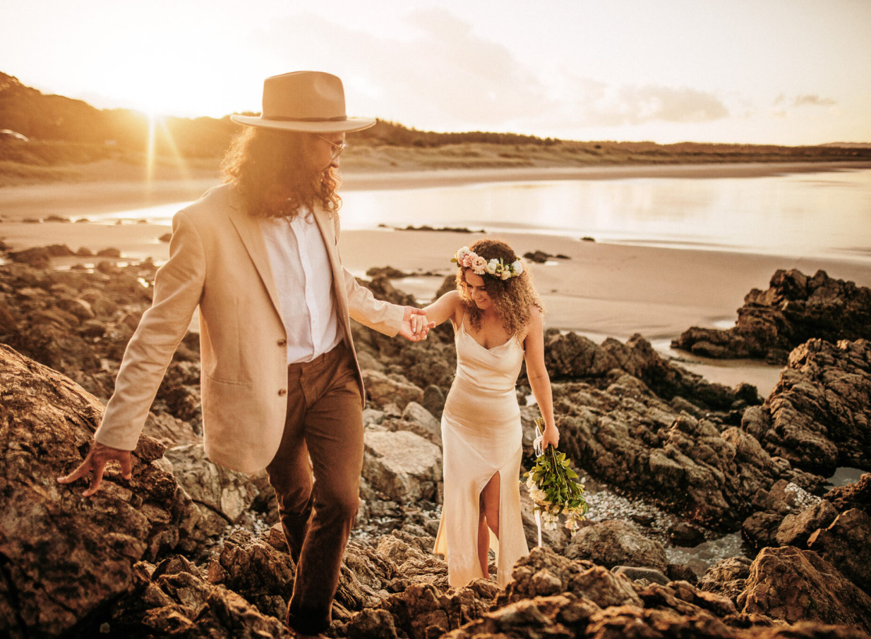 Auckland wedding photographer Zahn captures a couple's authentic beach moments on a rocky shore at sunset.