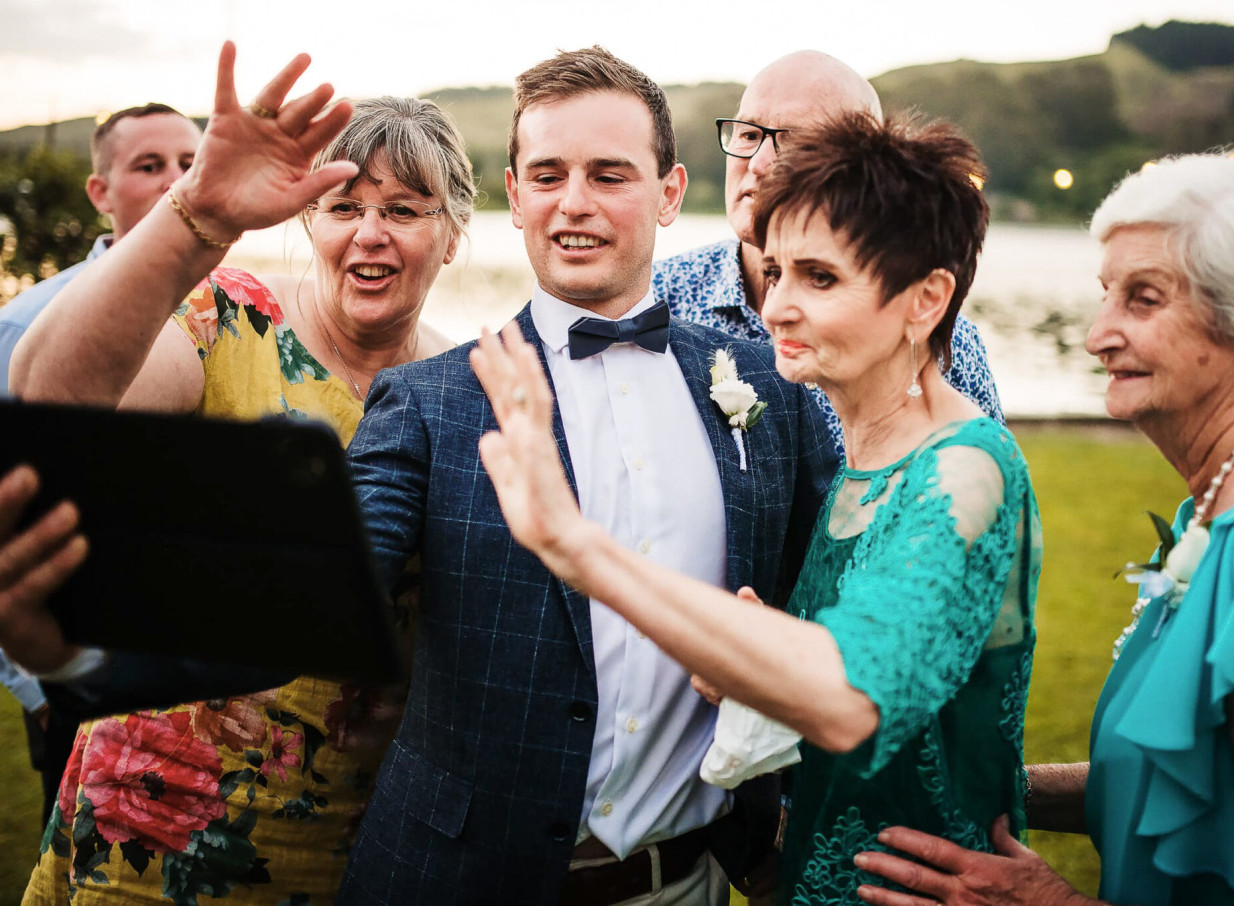 A candid outdoor wedding scene of a joyful group waving, reflecting Auckland photographer Zahn's focus on genuine moments.